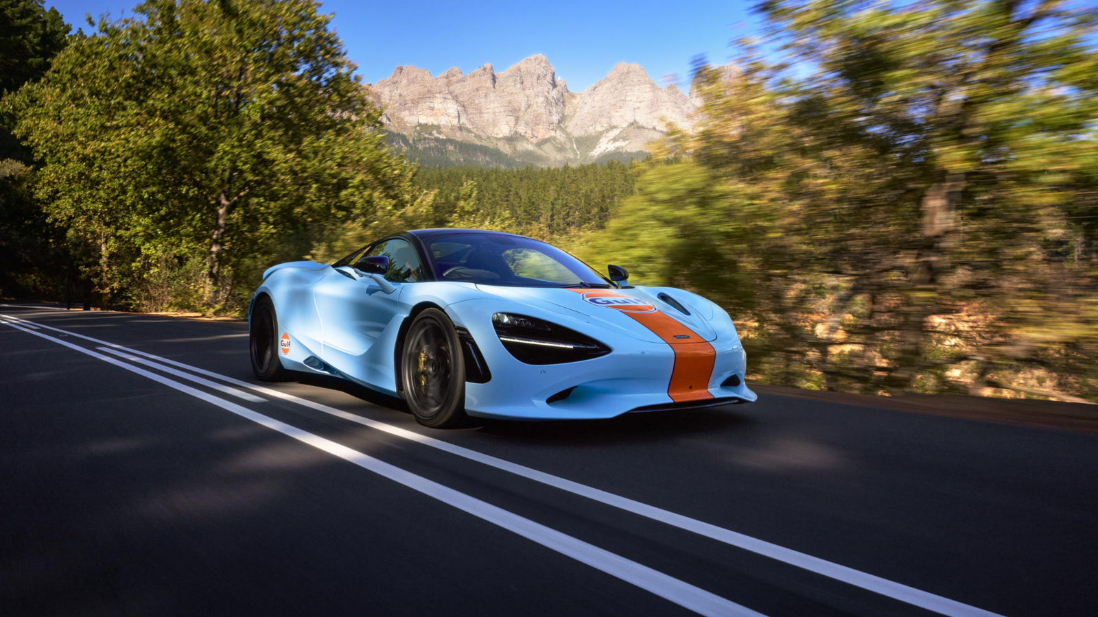 The McLaren and Gulf collab supercar driving at speed along a cliff top with hills in the background.