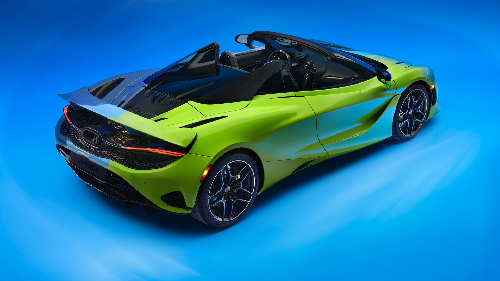 Inside the McLaren headquarters. On the left there is a row of McLaren cars lined up on display. Then to the left there are floor to ceiling windows that overlook the McLaren lake.