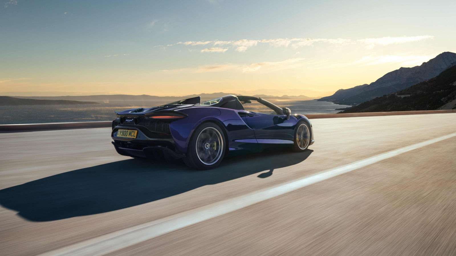 View of the McLaren Artura driving along a cliff top road with the sun beginning to set in the background.