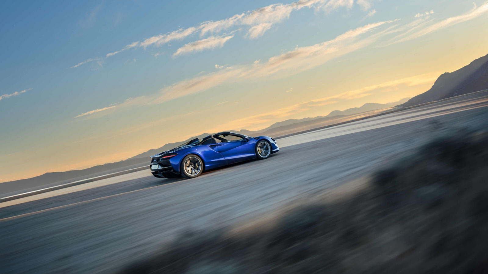 The McLaren Artura driving at speed with the sunsetting in the background.