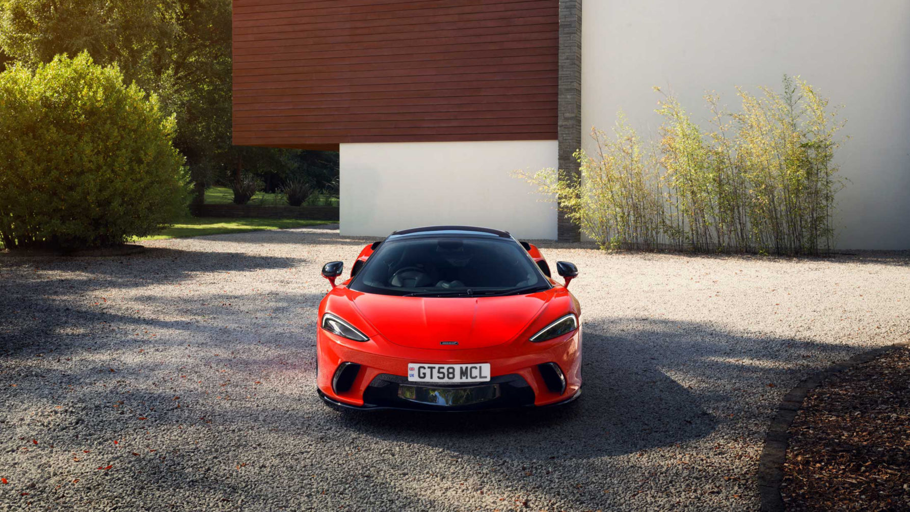 Landscape shot of the McLaren GTS in red parked on a stoney driveway.