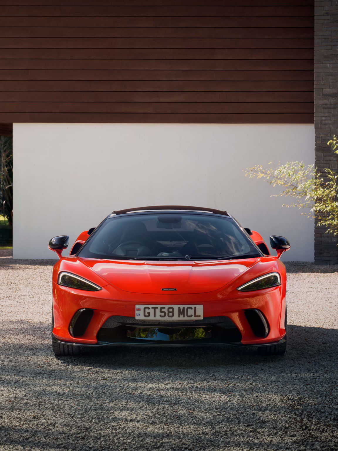 Portrait shot of the McLaren GTS in red parked on a stoney driveway.