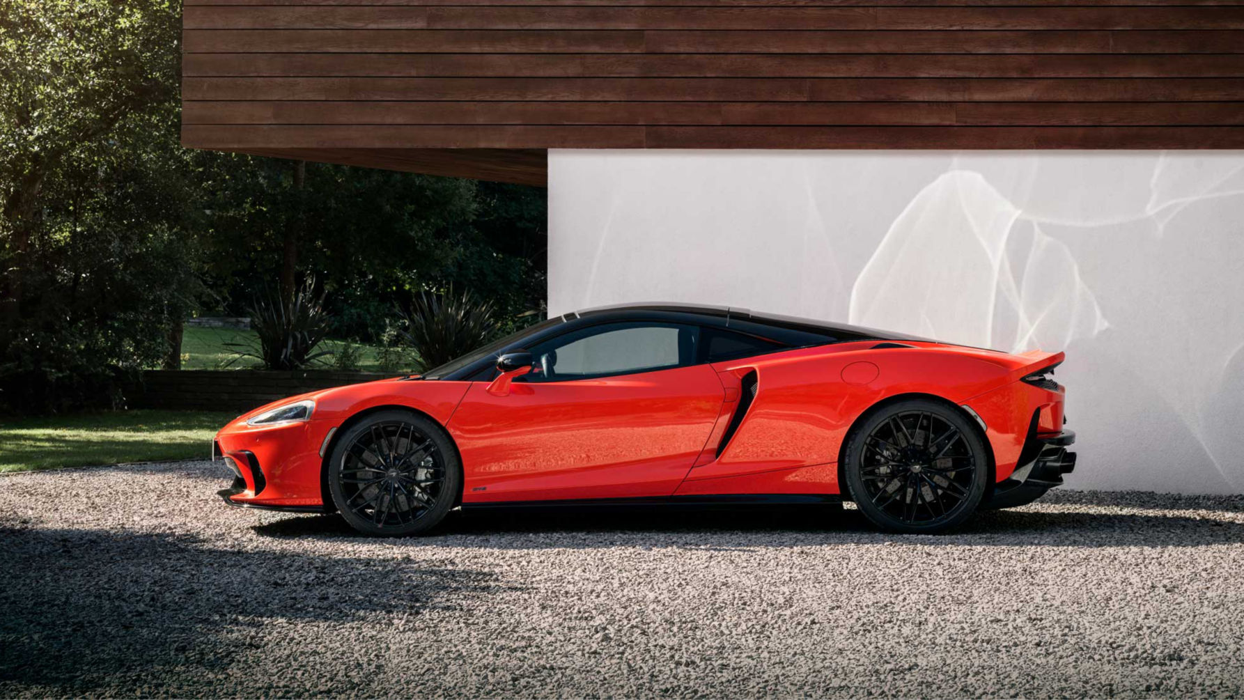 Landscape shot of the nearside of the McLaren GTS in red parked on a stoney driveway.