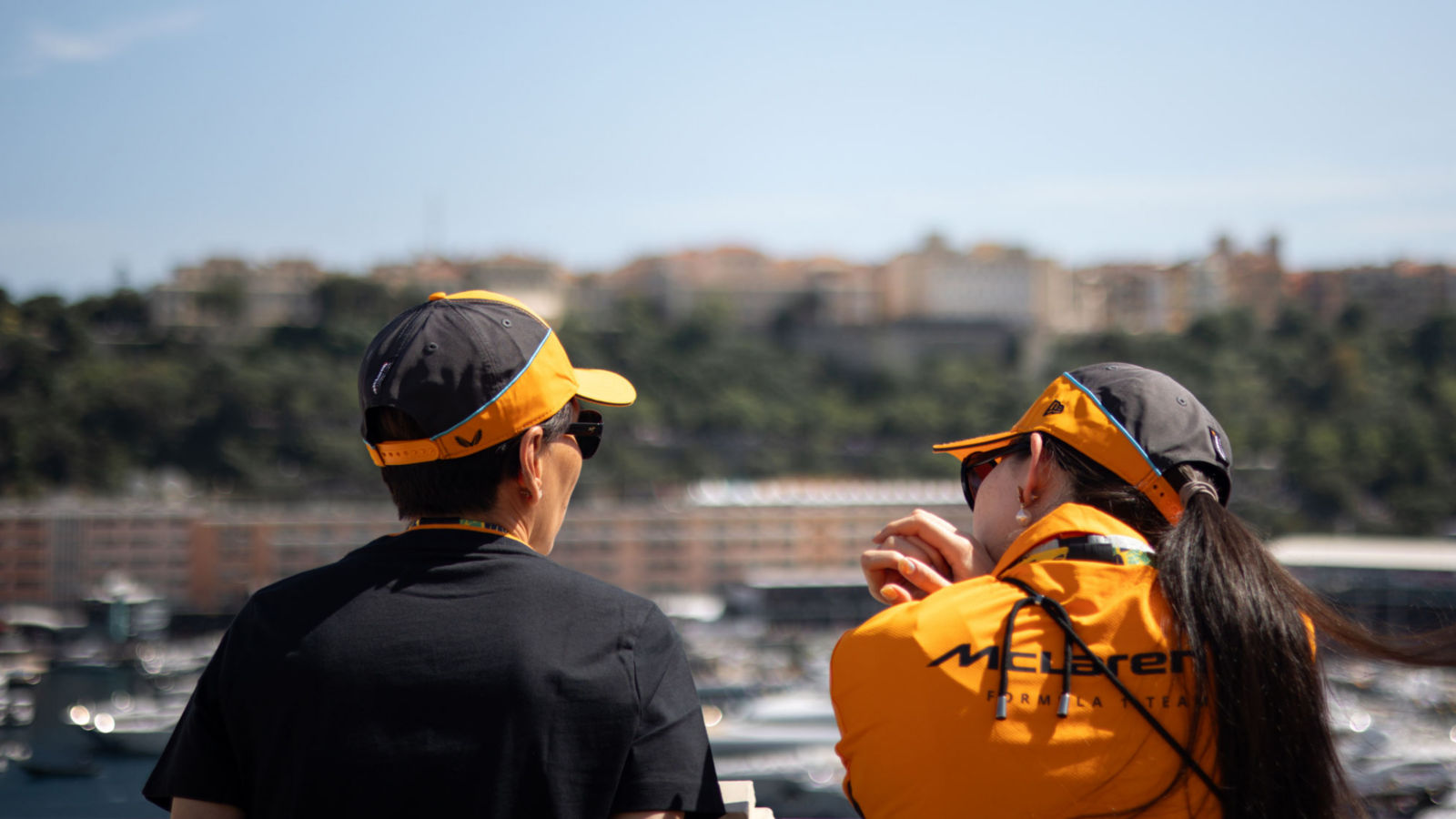 Two McLaren guests wearing McLaren merchandise, overlooking the Monaco harbour.