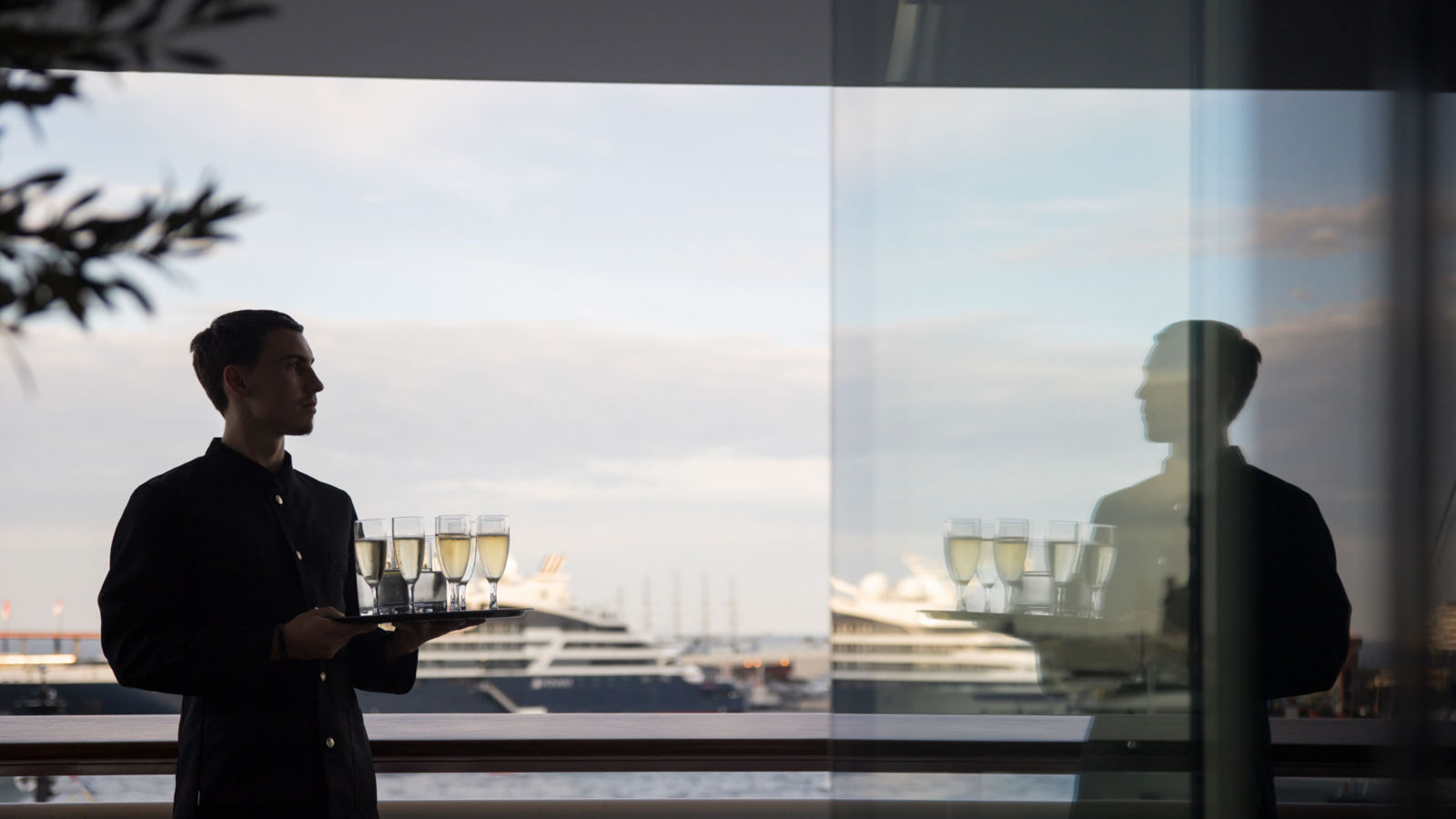 Waiter stood holding a tray of champagne glasses over looking the Mediterranean Sea.