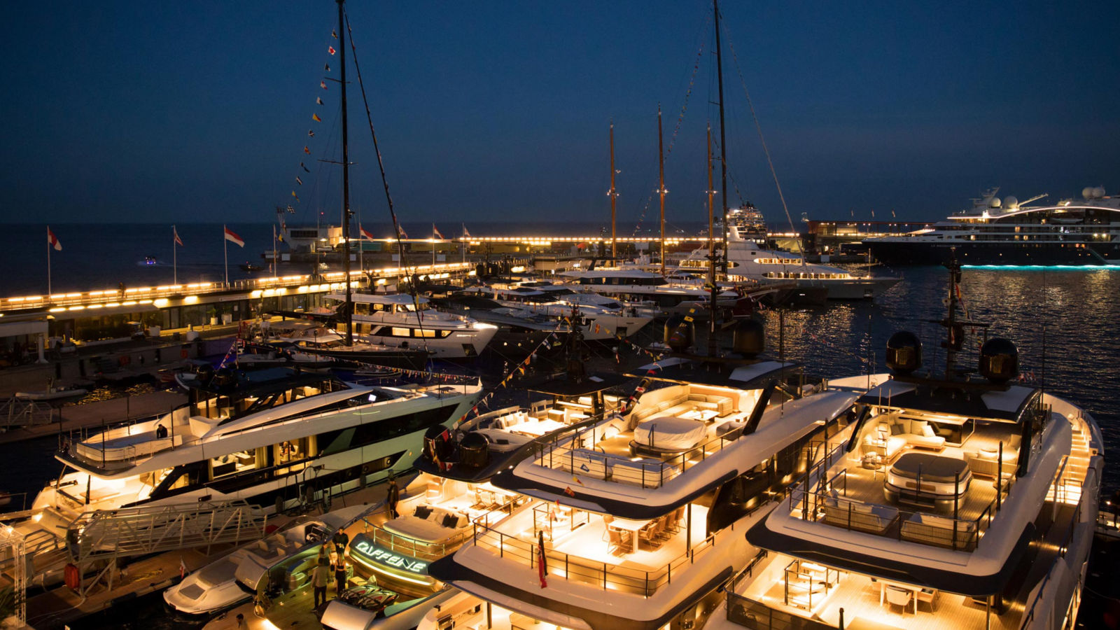 View of the Monaco Harbour at night showing multiple rows of docked Yachts.