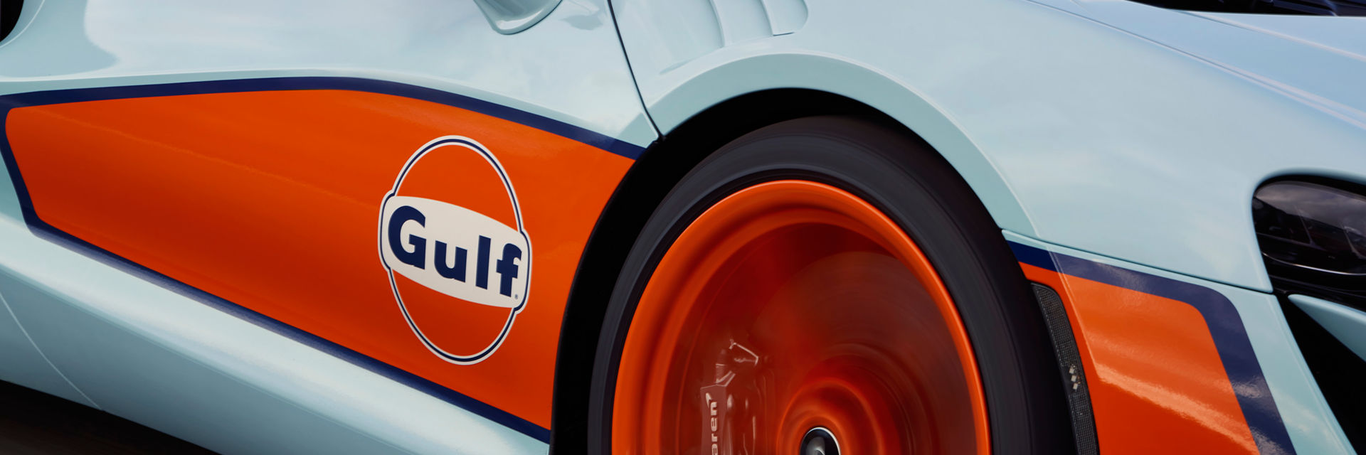 Photograph of the left side panel and wheel of the McLaren Artura with the Gulf branding. It has a orange stripe down the side with the Gulf logo.