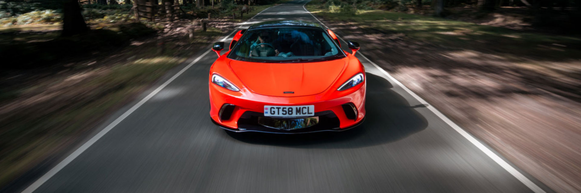 Landscape shot of the McLaren GTS in red driving through a forrest road.