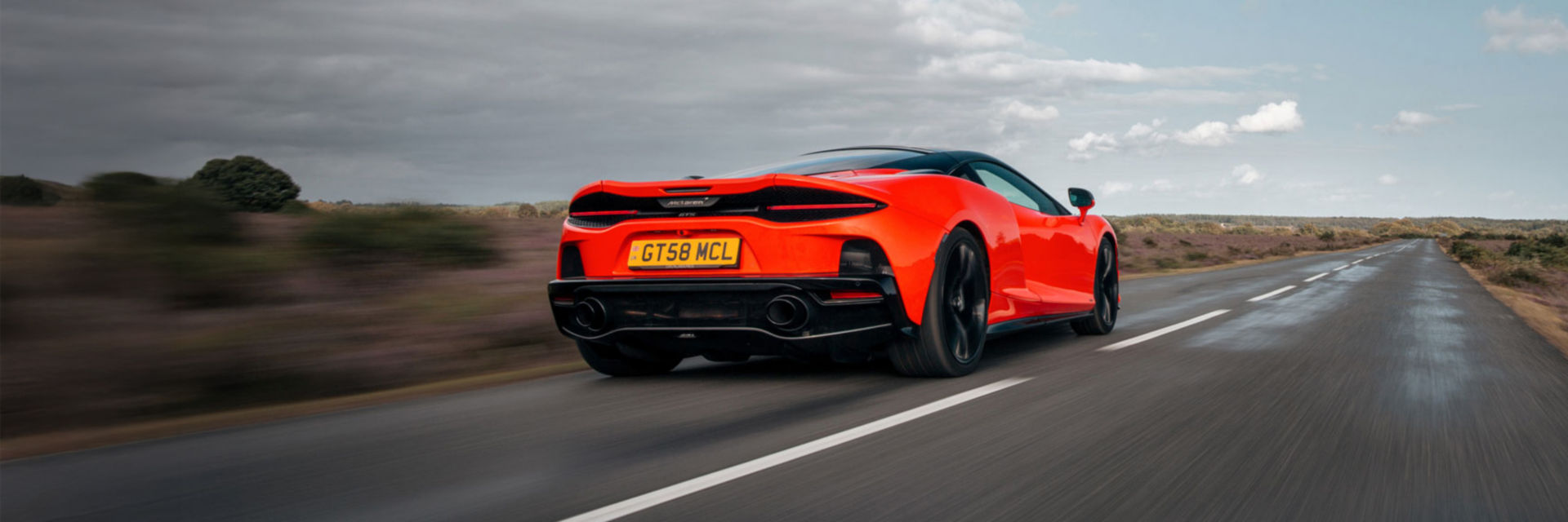 Landscape shot of the back of the McLaren GTS in red driving at speed along a country road.