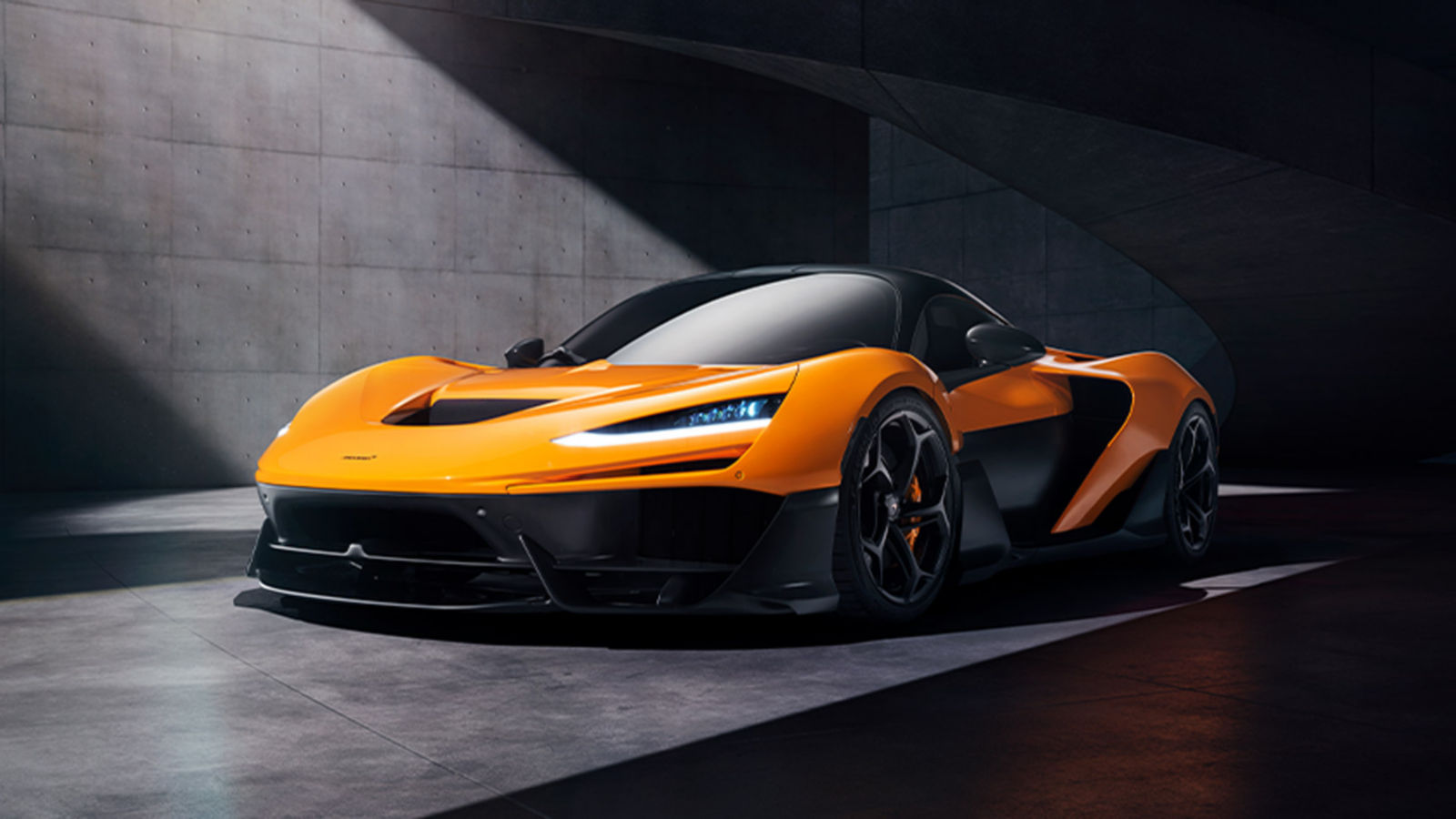 A 3/4 view of the front of a orange McLaren W1 standing out from the shadows.