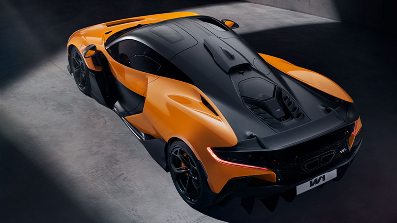 A high rear 3/4 image of an orange and black McLaren W1 in a dark environment with red rear lights illuminating.