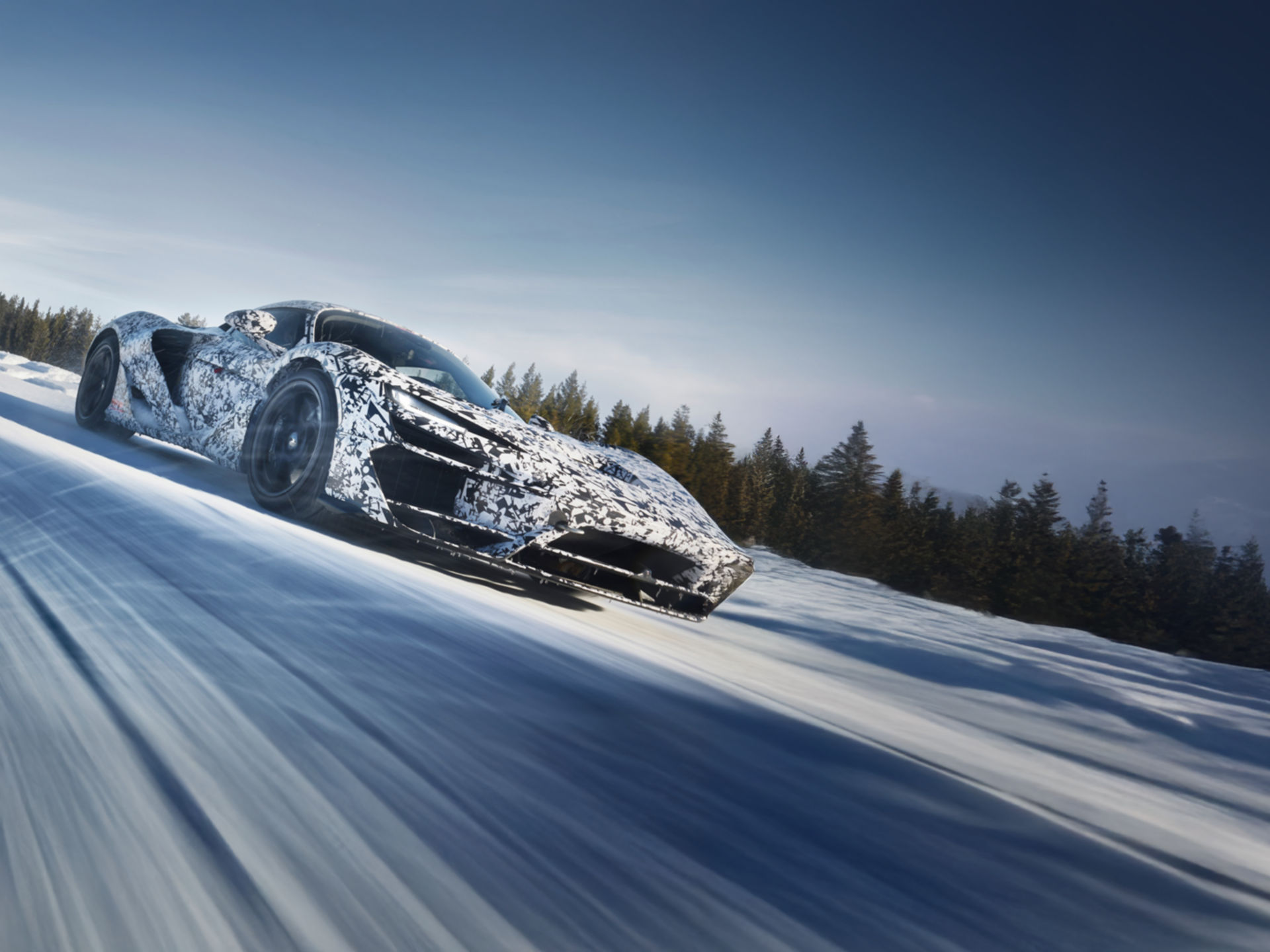 A camouflaged McLaren W1 prototype is speeding down a snow-covered road during winter testing, with motion blur indicating high speed.